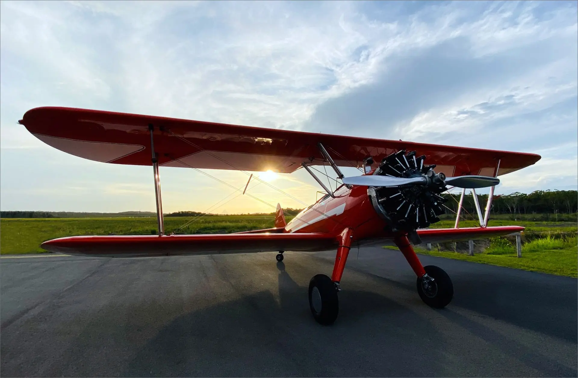 A grounded Stearman plane with a setting sun backdrop